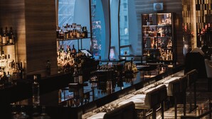 Een moderne bar met een hoge plafond, flessenkasten en een zithoek met stoelen.