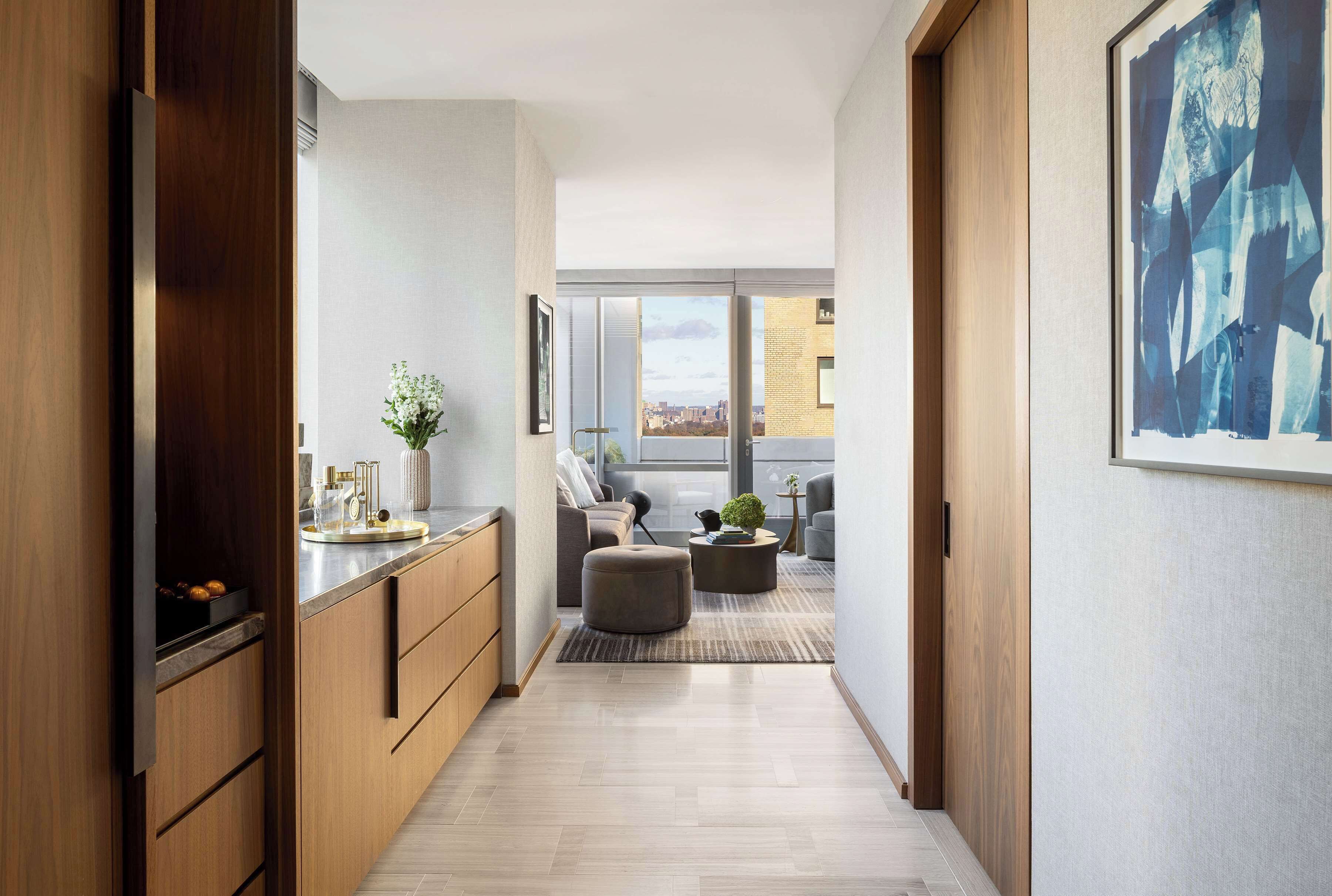A modern hallway with wooden cabinetry, a kitchen area, and a seating area with a view of the city.