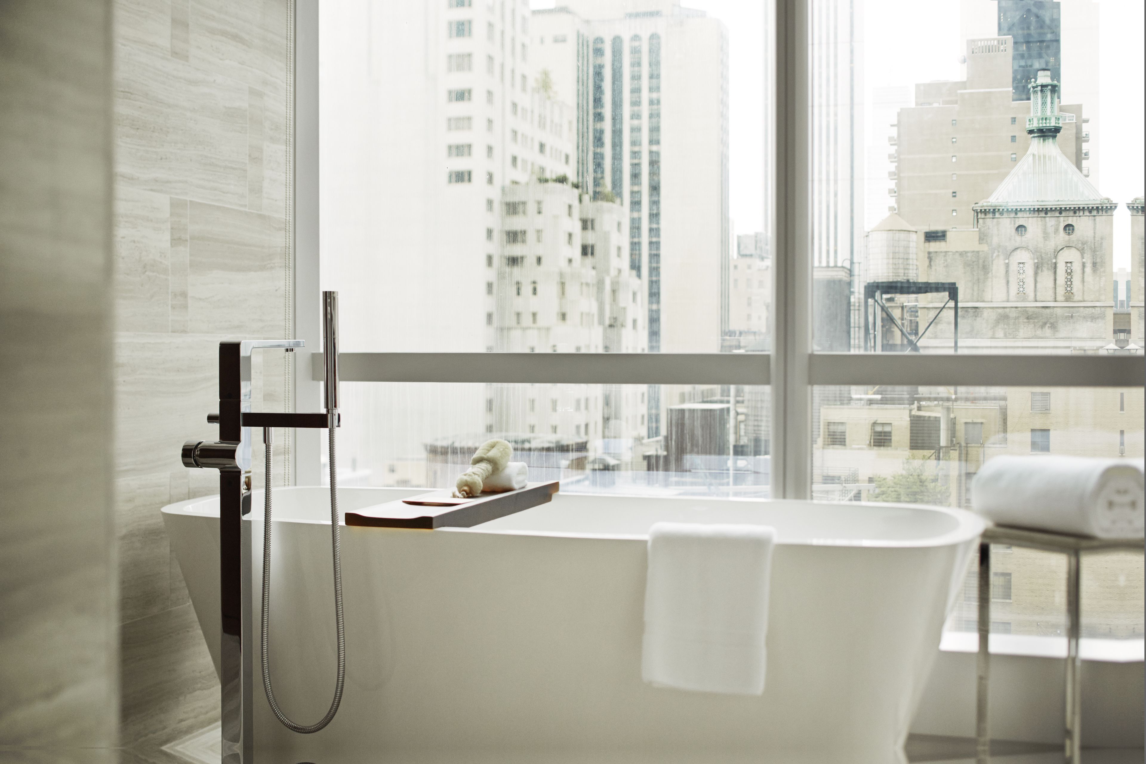 A modern bathroom with a freestanding bathtub, a towel rack, and a window overlooking a cityscape.
