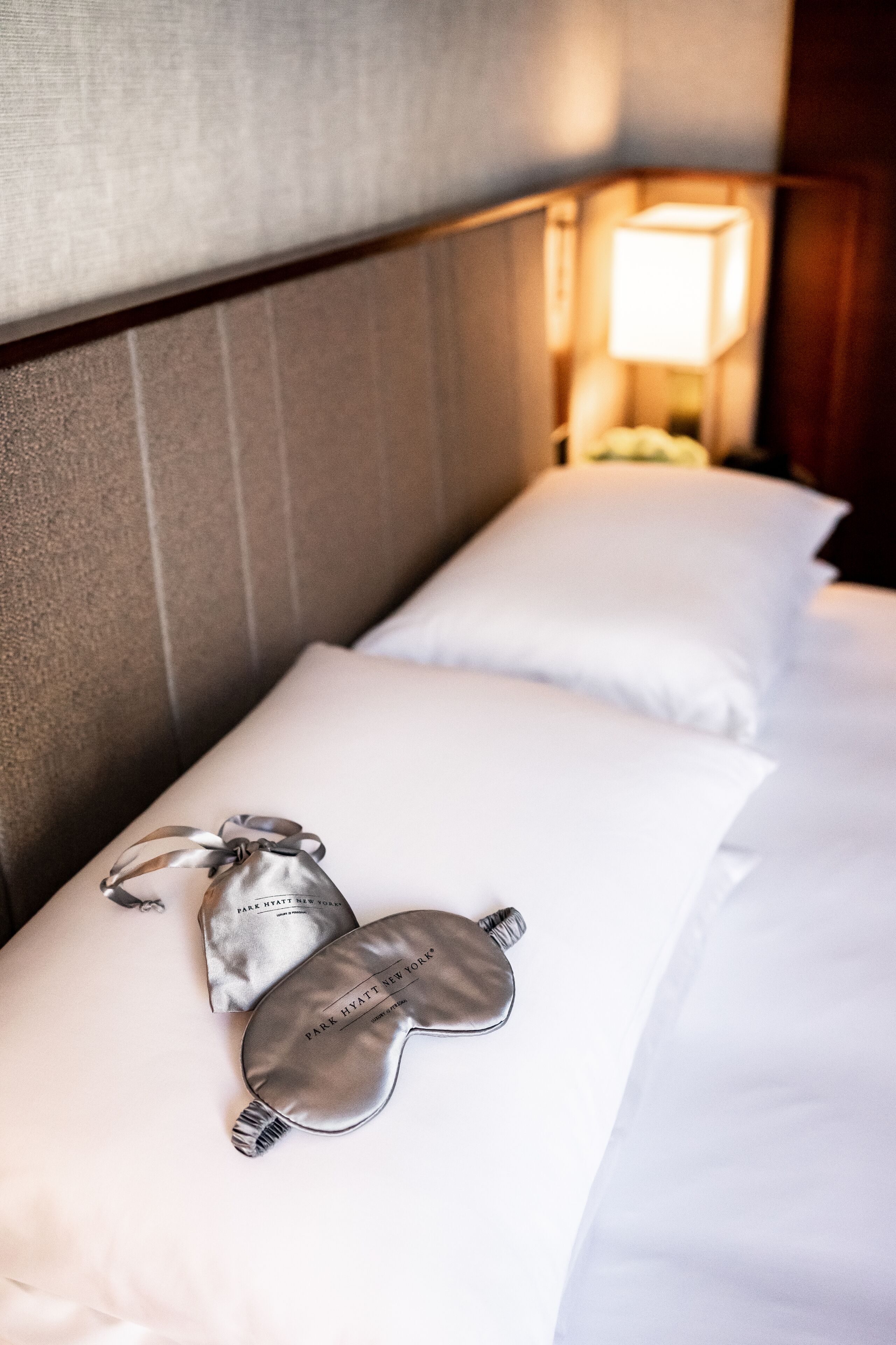 A neatly made bed with white linens and two eye masks on the pillows.