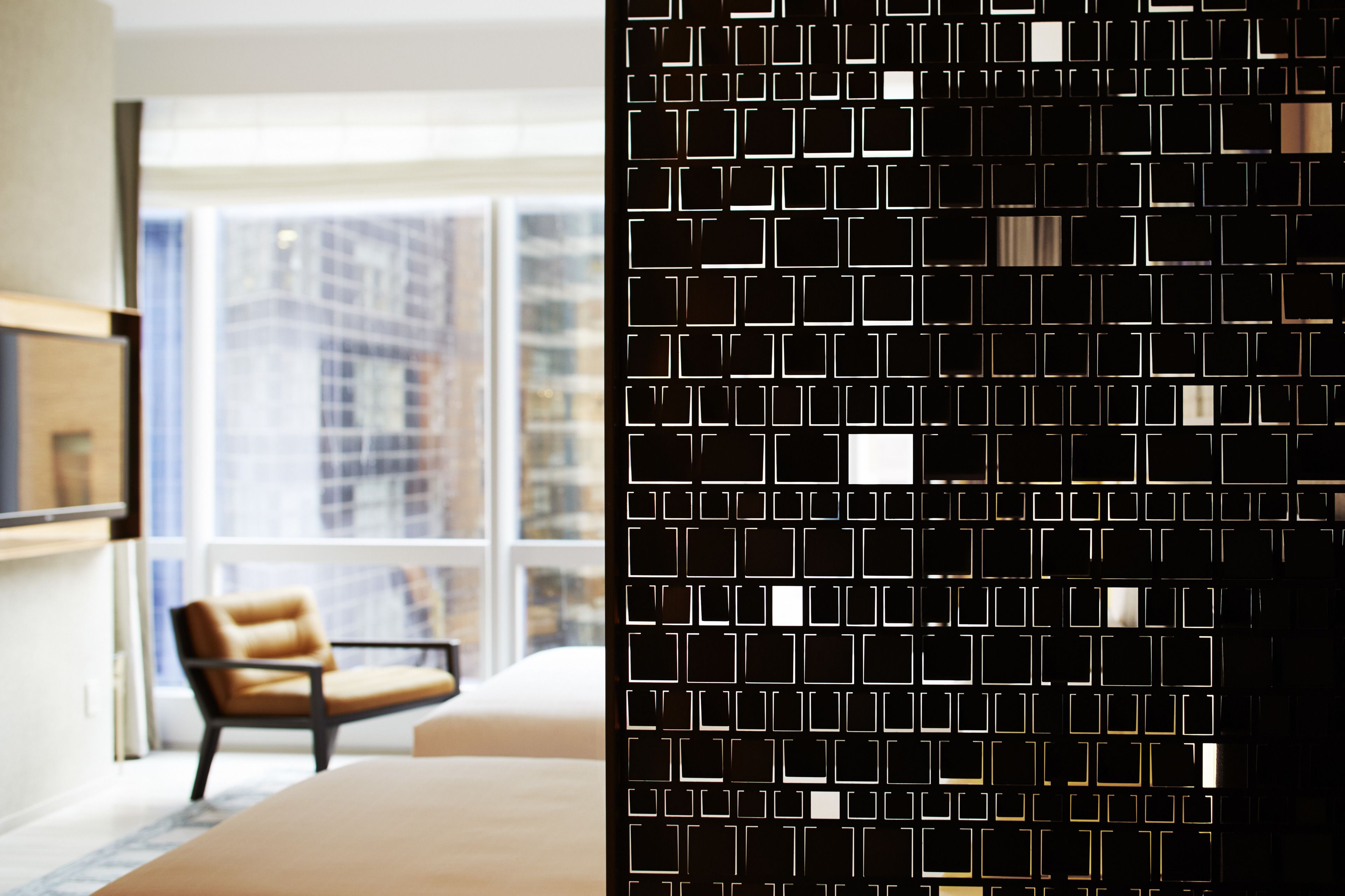 A modern hotel room with a large window, a brown leather chair, and a black patterned partition.