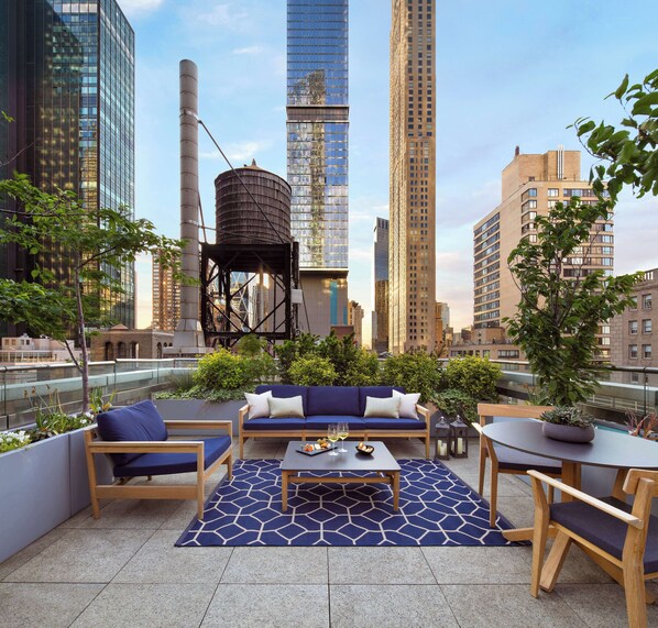 A rooftop terrace with a blue sofa set, wooden chairs, and a coffee table. - Park Hyatt New York (New York)
