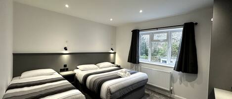 A modern bedroom with two beds, a window with black curtains, and a radiator.