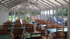 Un espace repas abrité, doté de tables et de chaises, de grandes fenêtres et d’un ventilateur de plafond.