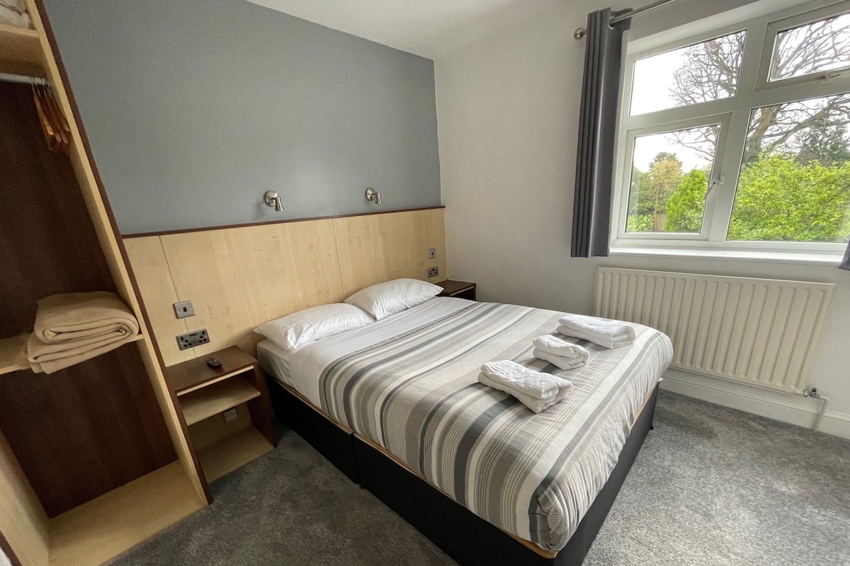 Une chambre à coucher comprenant un lit, une armoire en bois, une table de chevet, une fenêtre avec vue et un radiateur.