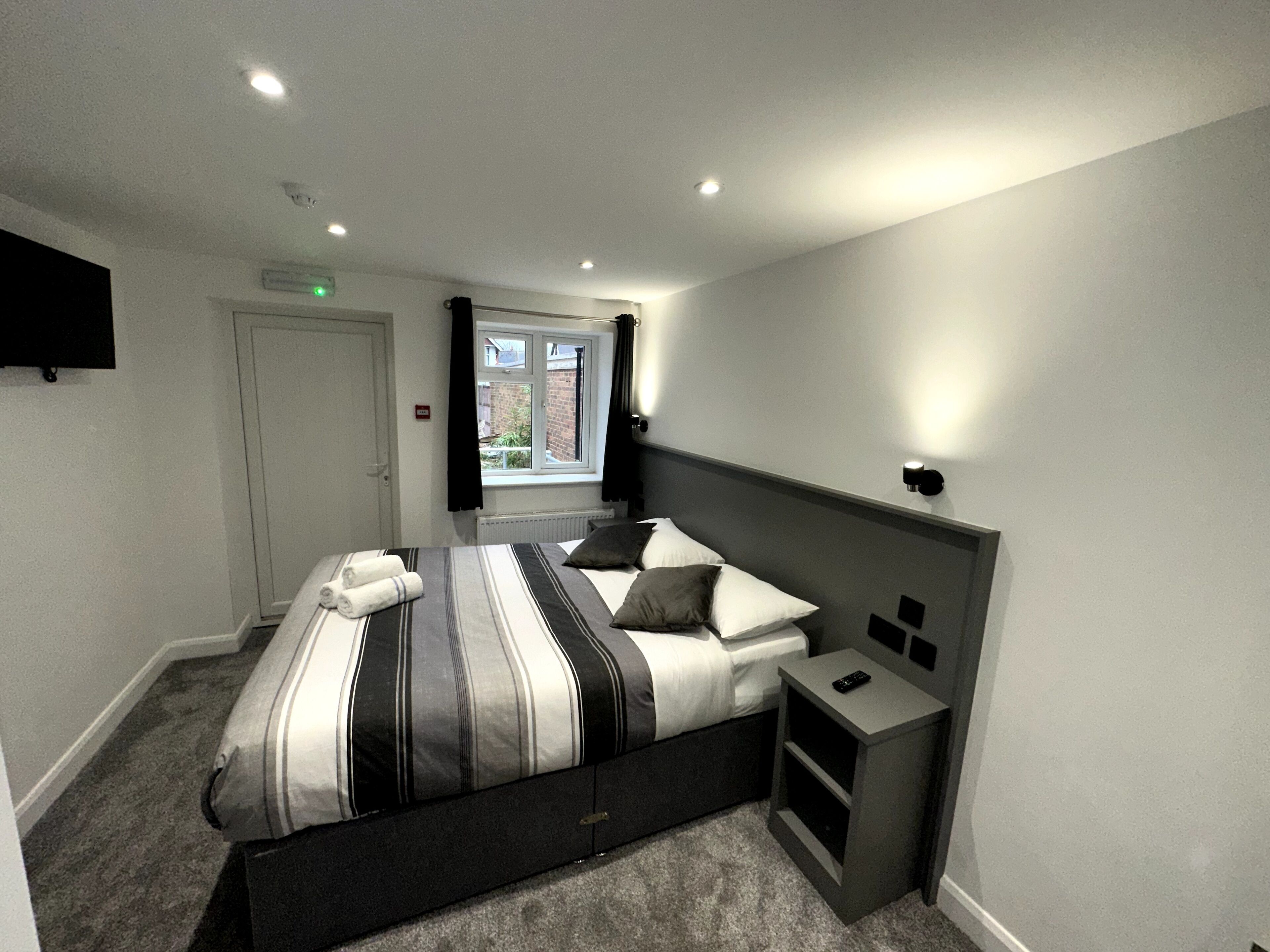 Ein modernes Schlafzimmer mit Bett, Nachttischen, Fenster und einem an der Wand befestigten Fernseher.