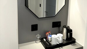 Une salle de bain avec un grand miroir octogonal, une machine à café, un plateau contenant des articles de toilette et un verre d’eau.