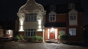 Un bâtiment à deux étages, doté d’une grande fenêtre en arc en plein cintre et d’une entrée illuminée.