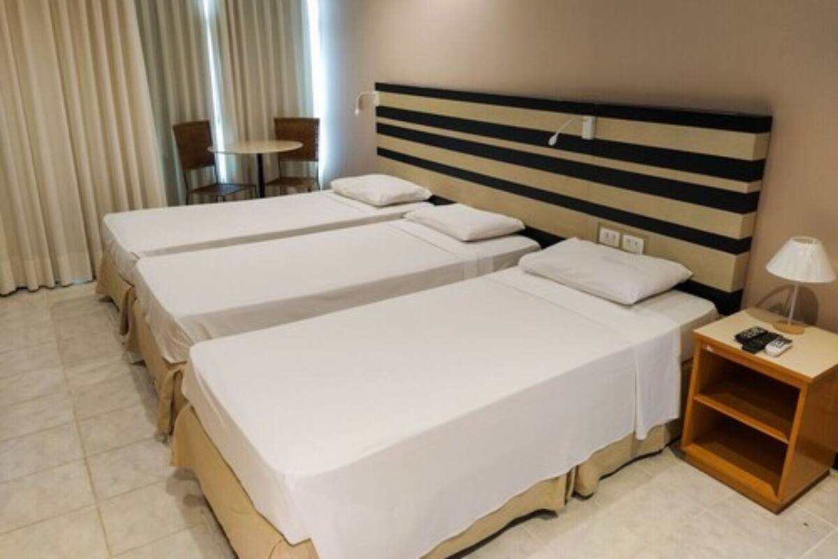Una habitación de hotel con dos camas individuales, una mesita de noche de madera, una lámpara y una silla.