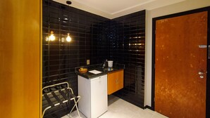 A compact kitchen with black tiled walls, a white refrigerator, wooden cabinets, and a small sink. - Savassi Village (Belo Horizonte)