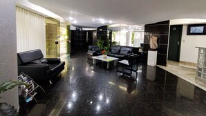 A modern lobby with black leather sofas, a coffee table, and a potted plant. - Savassi Village (Belo Horizonte)