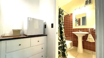 Un baño con lavamanos blanco, un espejo y una cortina de ducha con estampado de hojas.