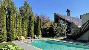 A swimming pool with a clear blue water, surrounded by green grass and tall trees. - Toll Road Inn (Manchester Center)