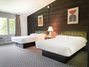 A hotel room with two beds, a nightstand with a lamp, a window with curtains, and artwork on the walls. - Toll Road Inn (Manchester Center)