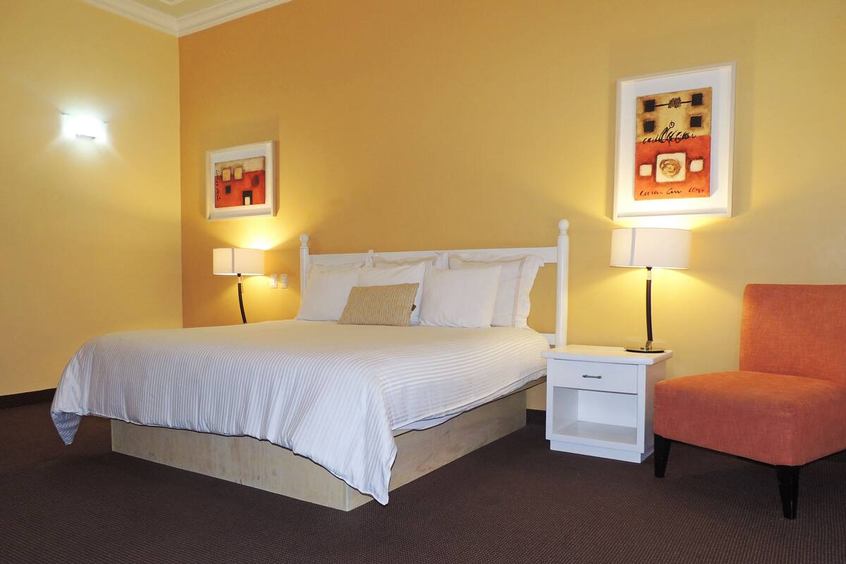 A hotel room with a bed, two bedside tables, a chair, and two wall-mounted lamps.