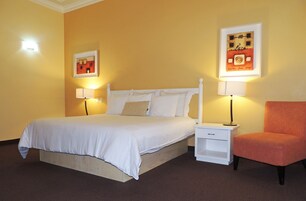 Una habitación de hotel con una cama, dos mesitas de noche, una silla y dos lámparas de pared.
