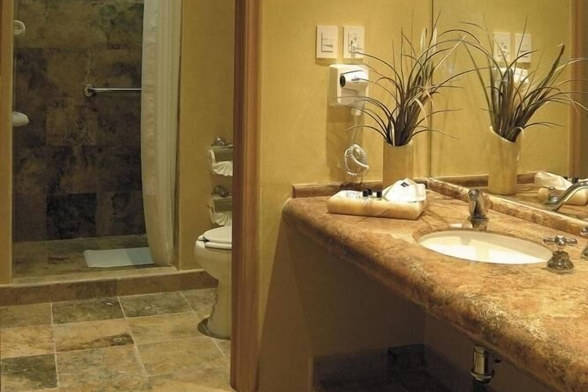 A bathroom with a stone shower, a sink with a marble countertop, and a mirror.