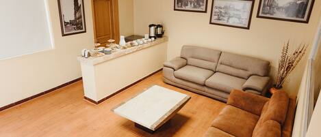 Sala de estar com sofá, mesa de centro, pequena cozinha com bancada e quadros nas paredes.