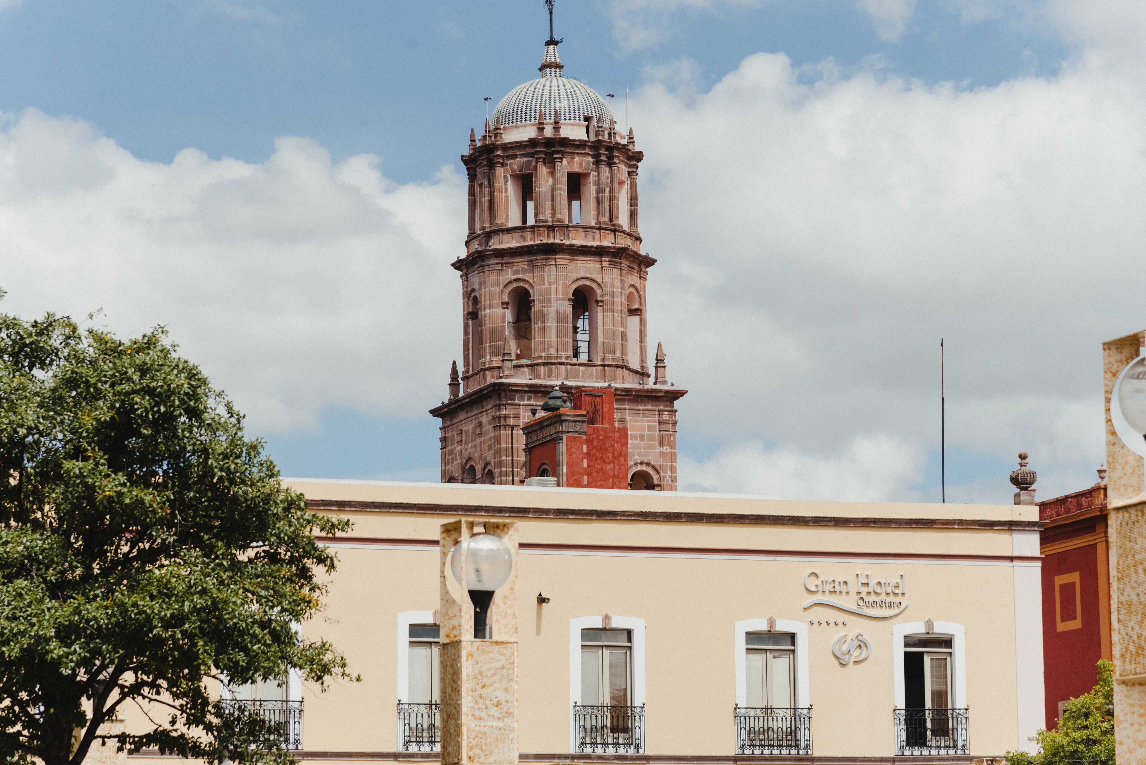 Un edificio histórico con una torre de campana, un letrero que dice Gran Hotel y un árbol en primer plano.