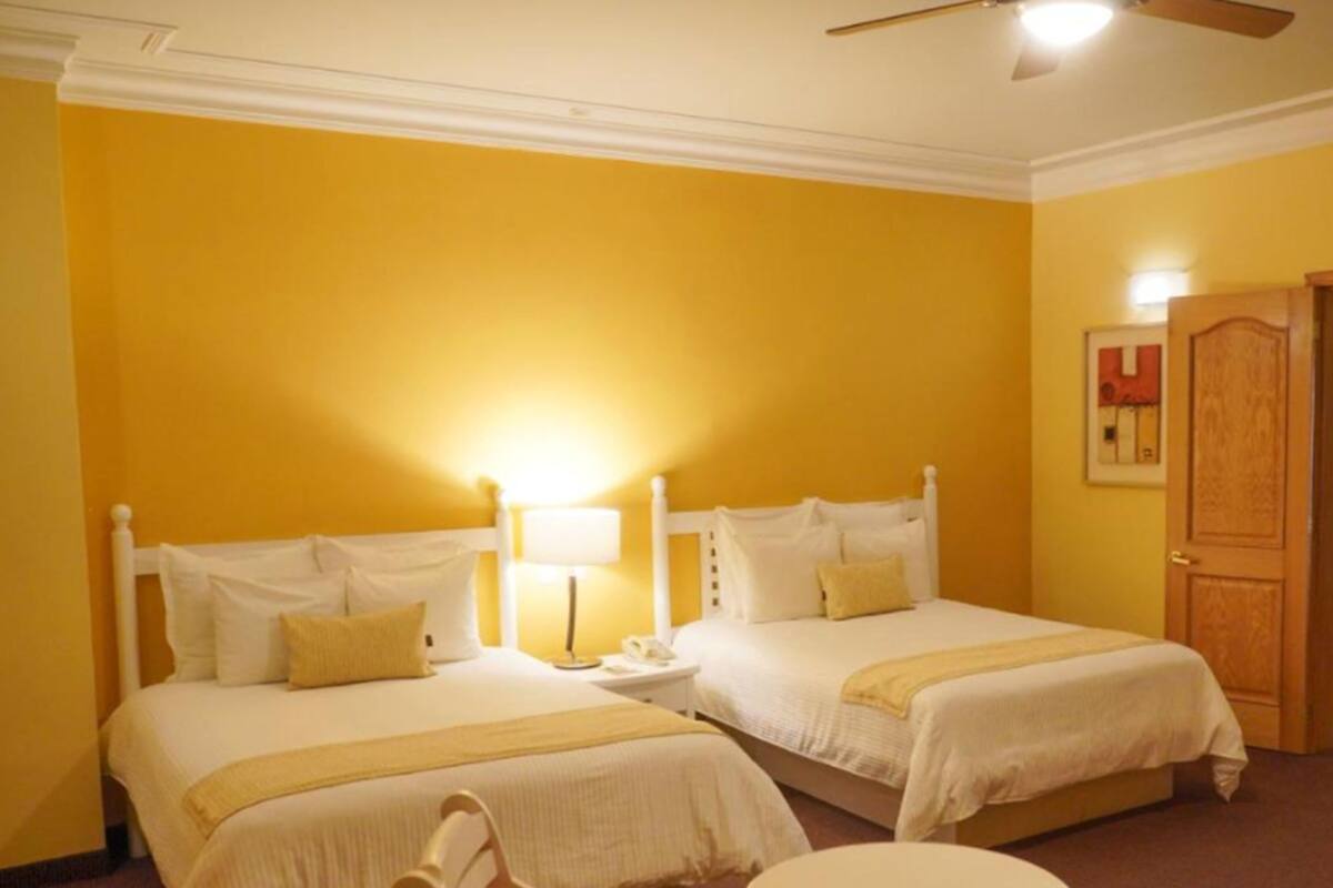 A hotel room with two beds, a small round table, and a ceiling fan.