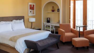 A hotel room with a bed, a desk, a chair, an ottoman, a ceiling fan, and a window.