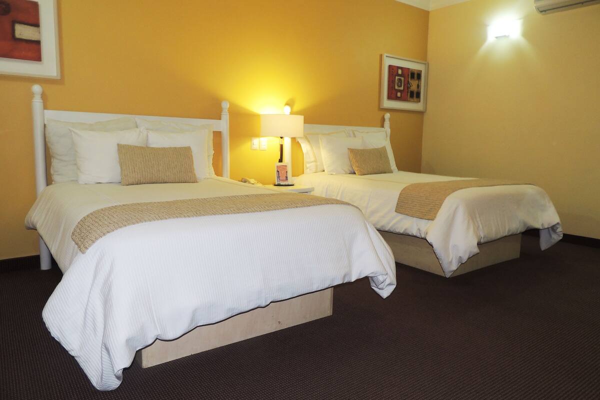 A hotel room with two beds, a nightstand with a lamp, and a framed picture on the wall.