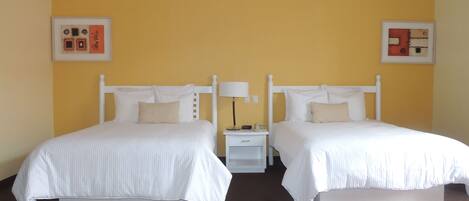 A hotel room with two single beds, a nightstand with a lamp, and two framed pictures on the walls.