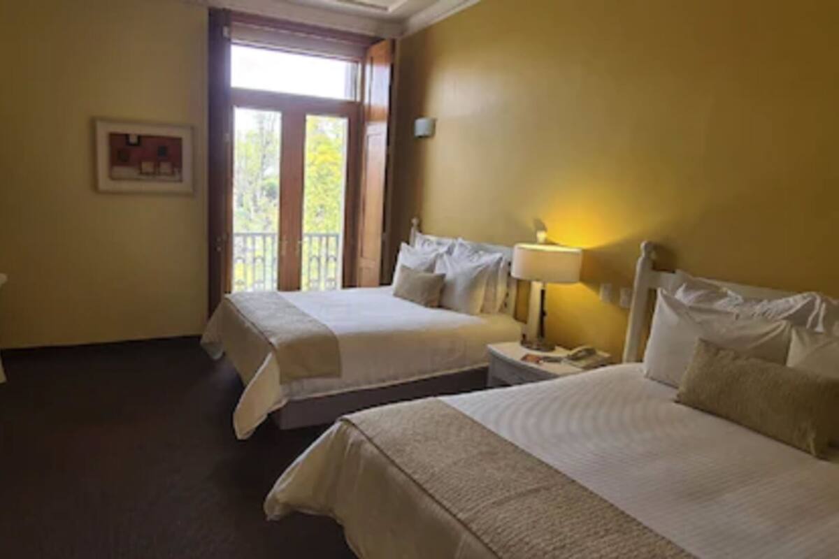 A hotel room with two beds, a chair, a nightstand, and a window with a view of trees.