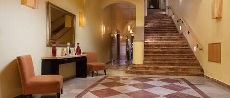 A spacious lobby with a checkered floor, a staircase, and a seating area with chairs and a desk.