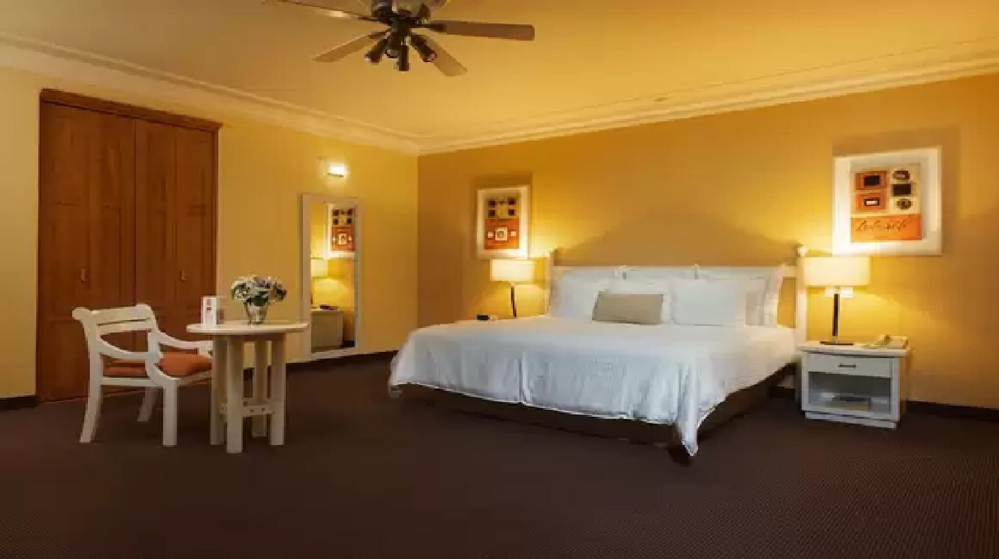 A hotel room with a bed, bedside tables, a chair, and a ceiling fan.