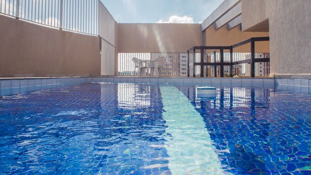 A swimming pool with clear blue water, surrounded by a modern building with large windows and a balcony. - Guara Inn (Guaratingueta)