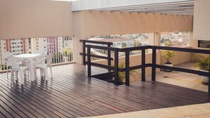 A balcony with a wooden floor, white plastic chairs, and a black railing. - Guara Inn (Guaratingueta)