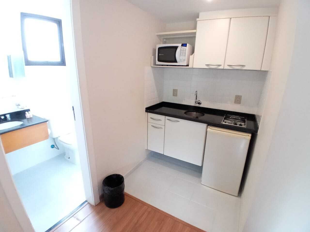 Una cocina compacta con armarios blancos, encimera negra, microondas y un refrigerador pequeño.