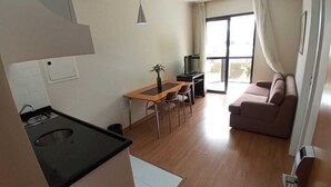 A compact living space with a kitchenette, a dining area, a sofa, and a large window. - Guara Inn (Guaratingueta)