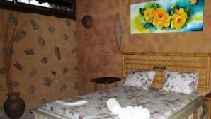 Un dormitorio con una cama de patrón de piedra, cabecera de madera, un cuadro de flores amarillas en la pared y un jarrón a la izquierda.