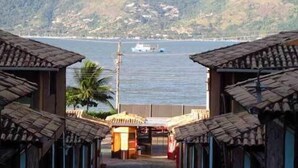 Una hilera de edificios de madera tradicionales con vista a un mar tranquilo y colinas lejanas.