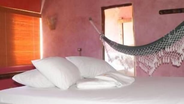 Una cama con ropa blanca, una hamaca y una ventana con persianas.