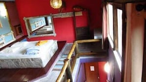 Una habitación con una cama, una escalera de madera, una pared roja y una lámpara colgante.