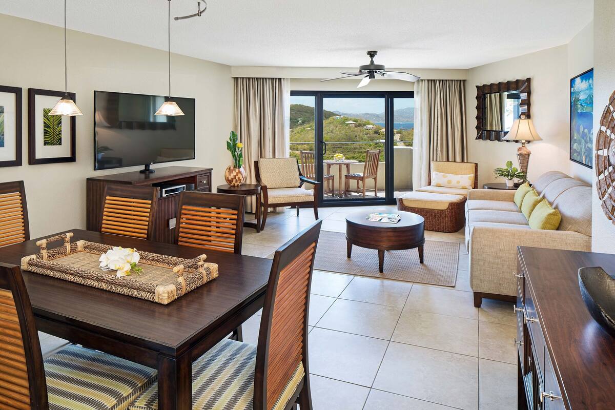 Una habitación de hotel moderna con comedor, sofá, televisor y balcón con vistas.