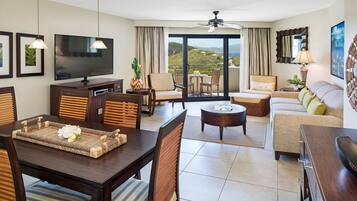 A modern hotel room with a dining area, a sofa, a TV, and a balcony with a view.