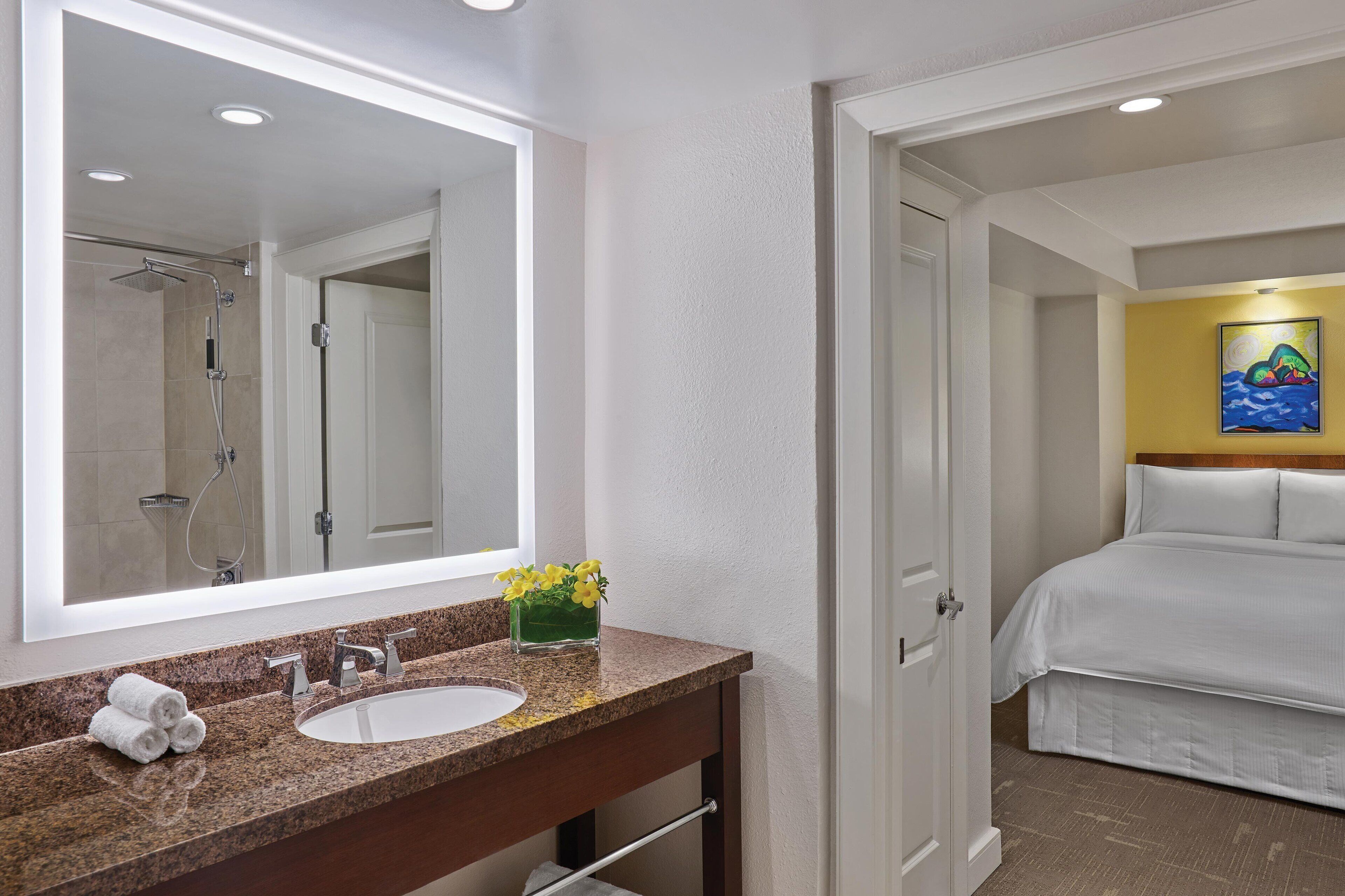 A hotel bathroom with a large mirror, a sink, and a shower.