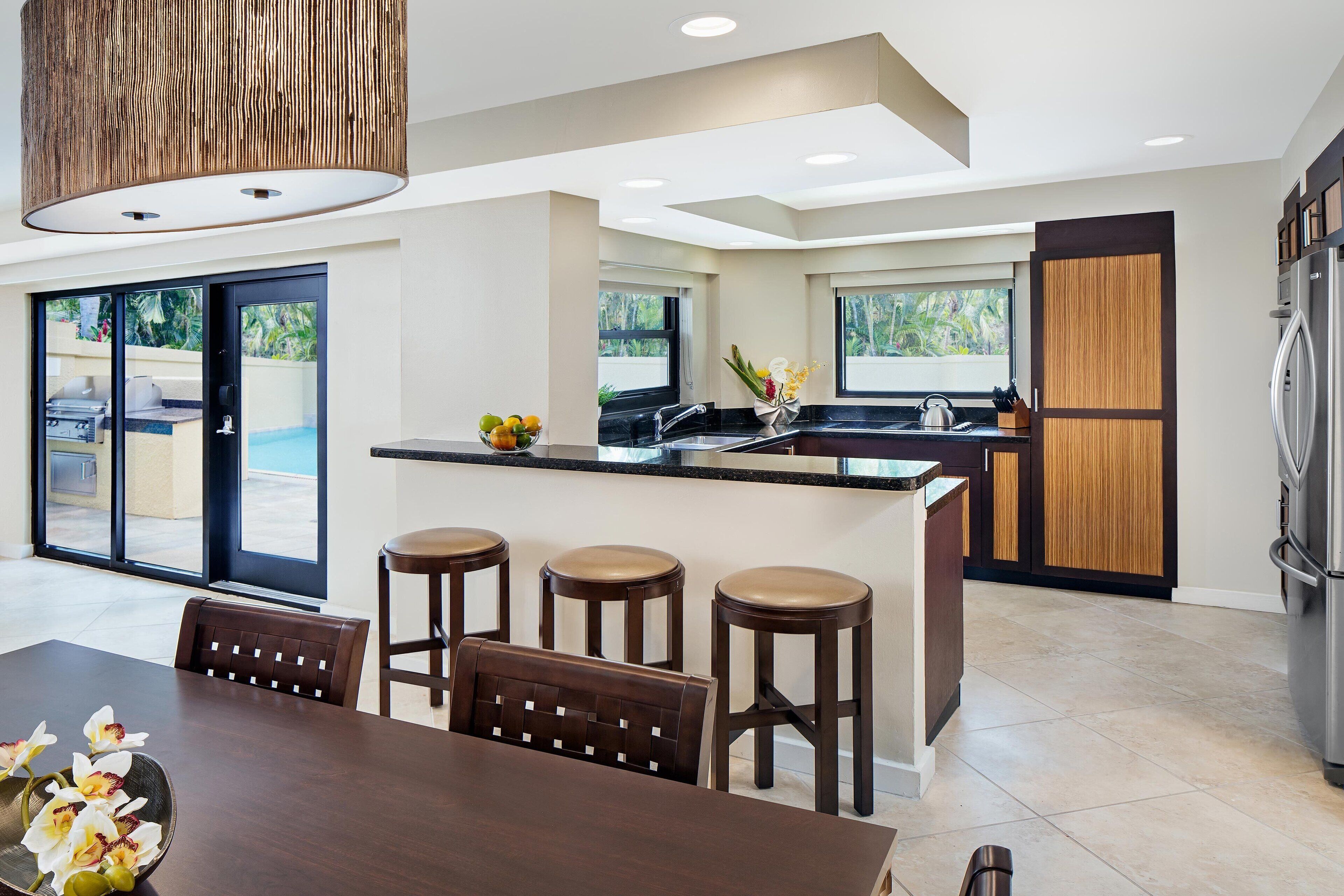 A modern kitchen with a central island, bar stools, and a dining area with a table and chairs.