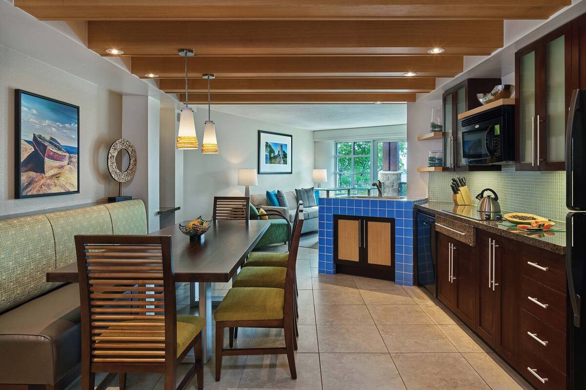 Una cocina moderna con armarios de madera, salpicadero de azulejos azules y una zona de comedor con mesa y sillas de madera.
