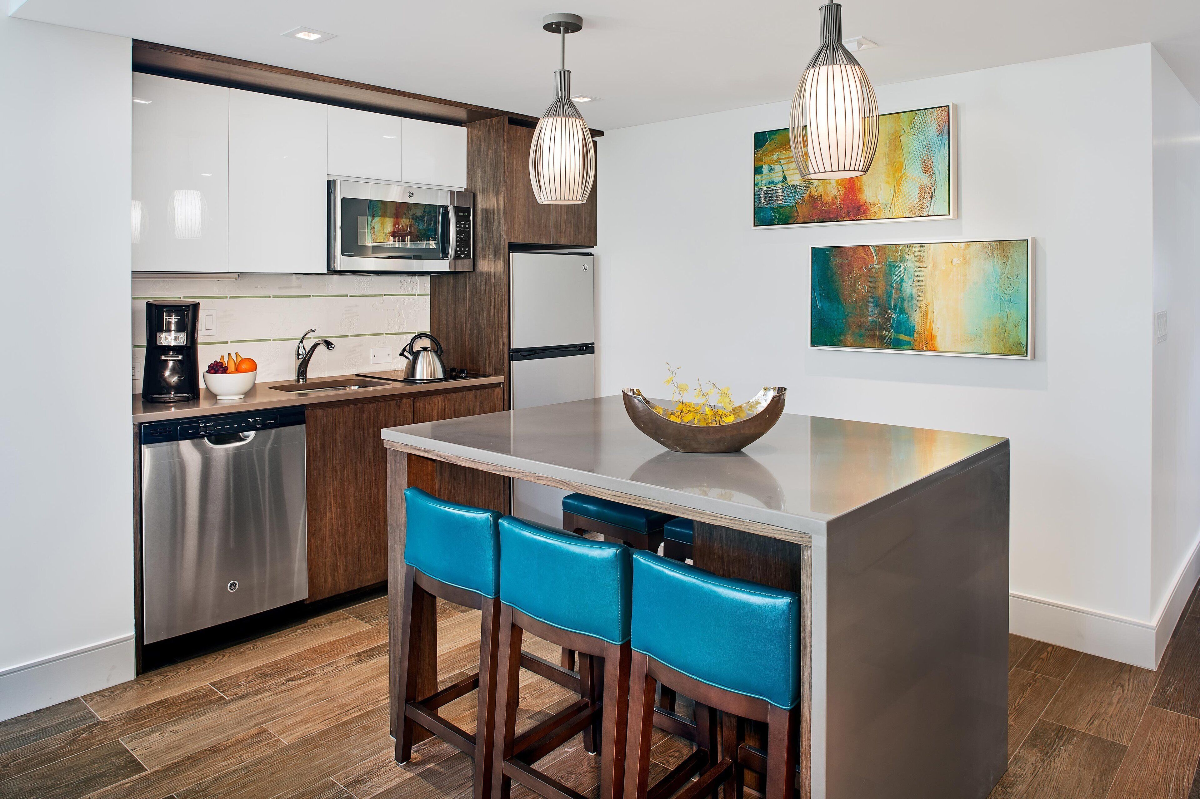 A modern kitchen with a central island, bar stools, stainless steel appliances, and abstract wall art.