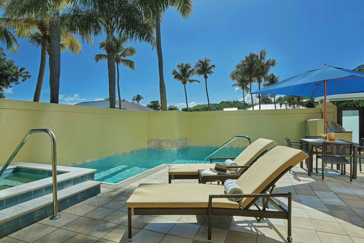 Un área junto a la piscina con sillones de descanso, una piscina y palmeras.