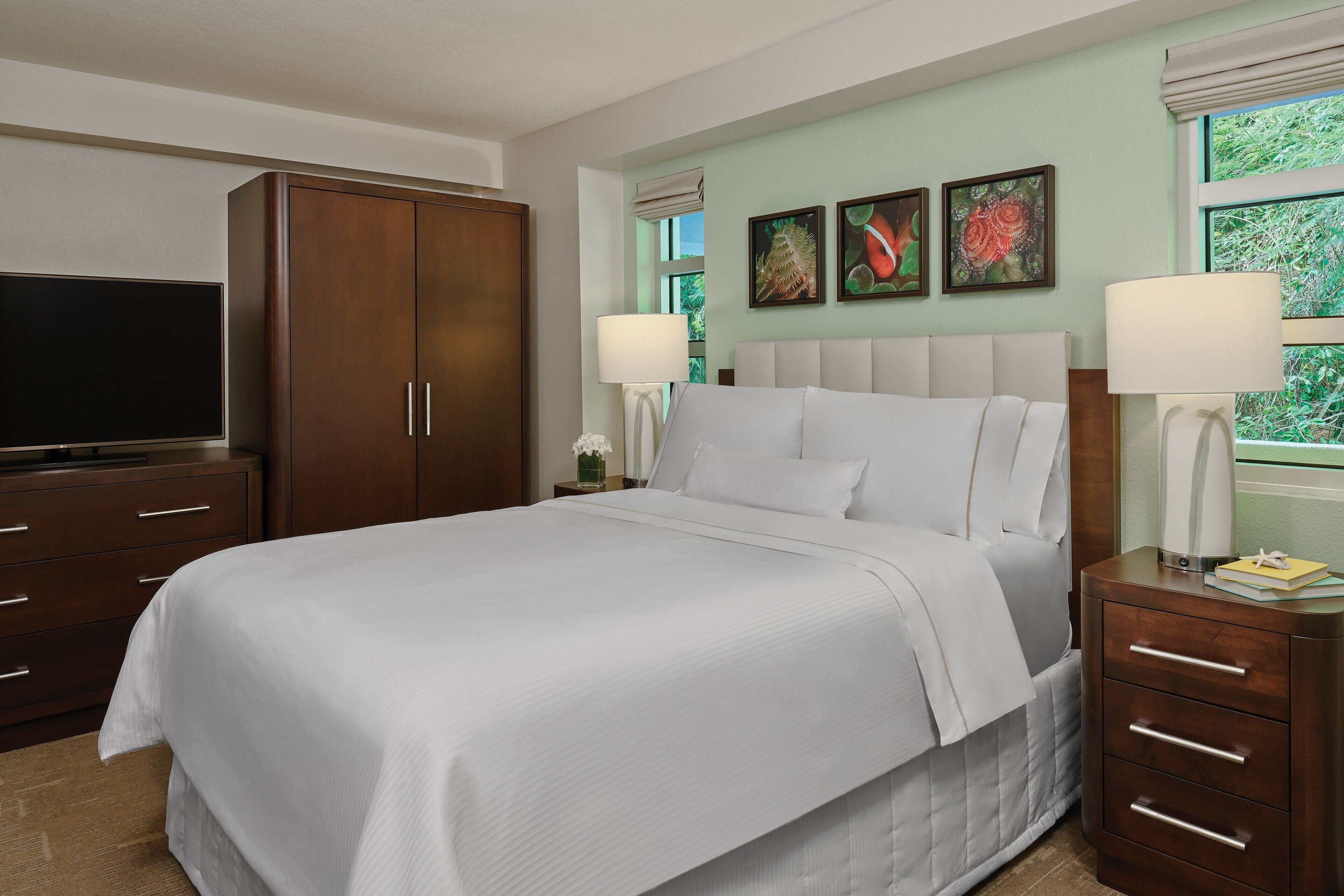 A hotel room with a large bed, a TV, a wardrobe, and artwork on the wall.