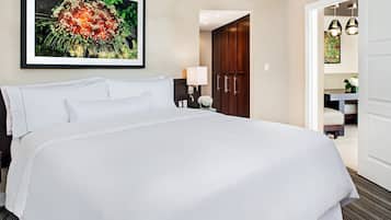 Een hotelkamer met een groot bed, een lijst met bloemenkunst boven het bed, een bureau met een lamp en een zichtbare badkamer door een open deur.