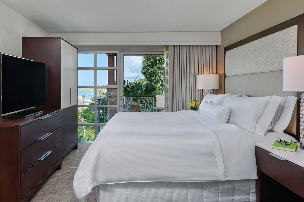 Habitación de hotel con una cama grande, televisión, escritorio con lámpara y vistas al exterior.