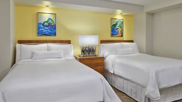 A hotel room with two beds, a nightstand with a lamp, and two paintings on the wall.