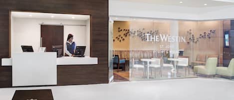 A reception area with a receptionist, a desk, and a glass partition displaying a seating area.